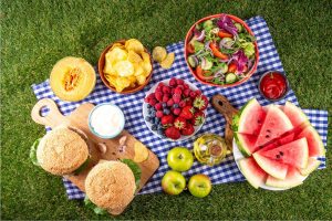 Healthy summer snacks including fruits, vegetables, yogurt, and cheese arranged for a family picnic.